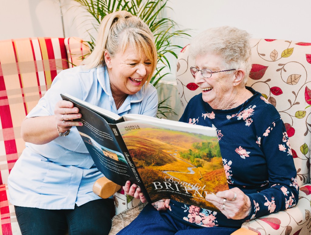 A caregiver and resident sharing a laugh over a picture book together